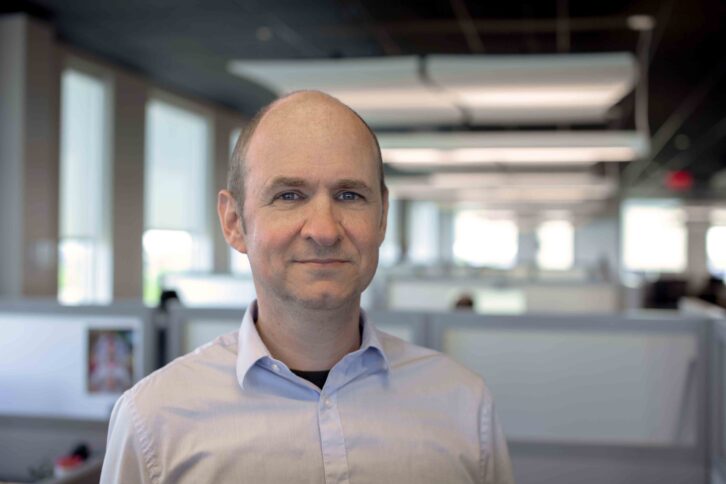 Mark Horchler wears a white shirt and stand in front of a traditional office layout